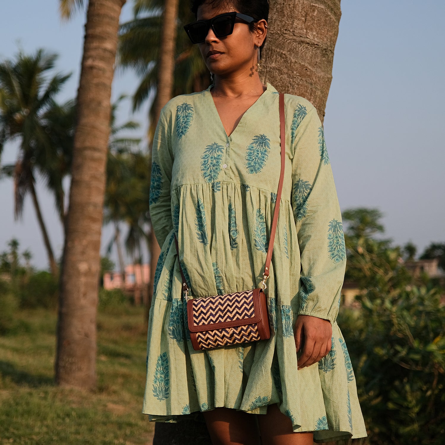 Woman in a light green dress with pineapple patterns standing under a palm tree.
